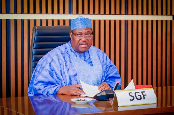SGF George Akume seated at a desk with an SGF name sign